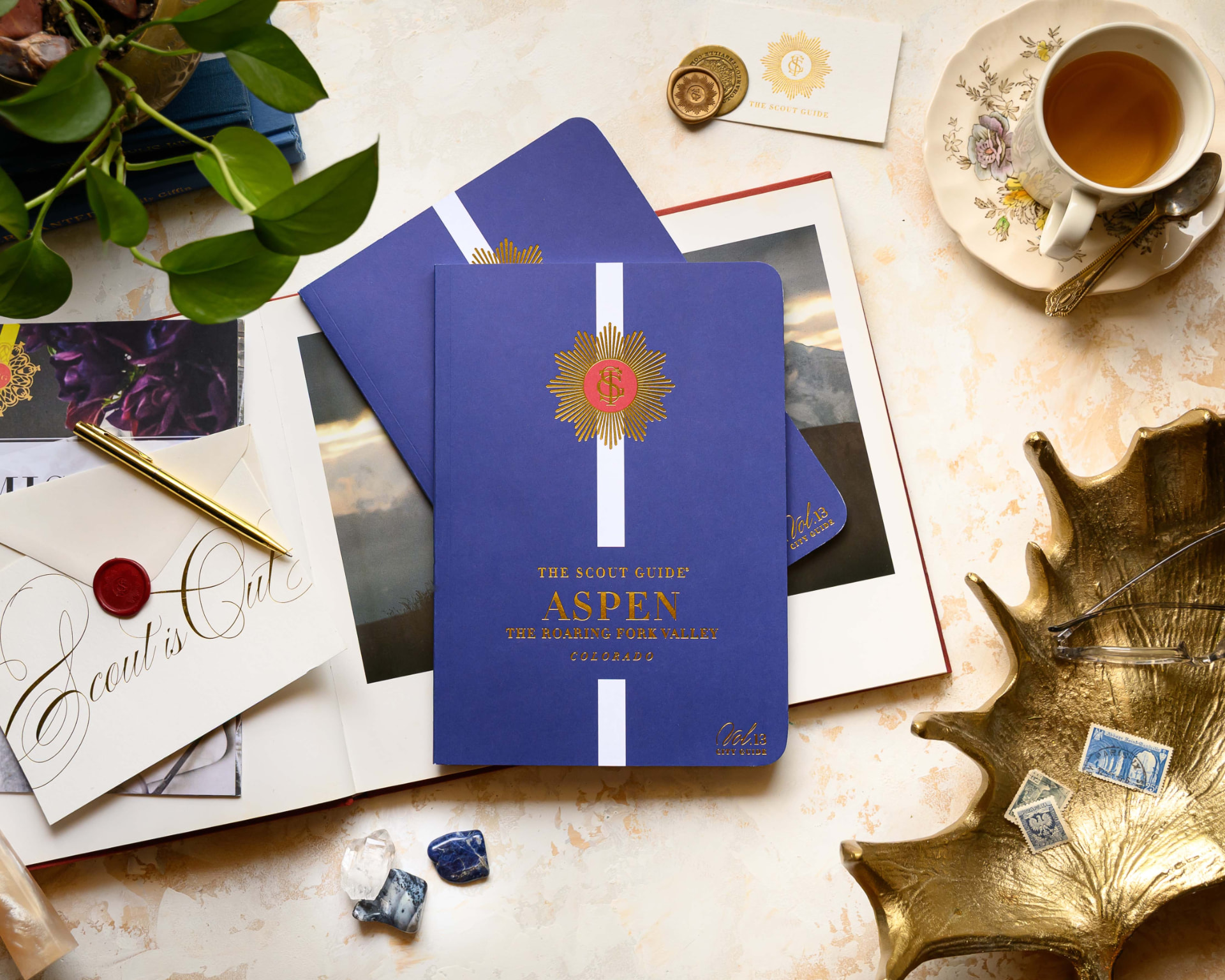 The Scout Guide Aspen Volume 13 notebooks, gold pen and tea on a marble surface